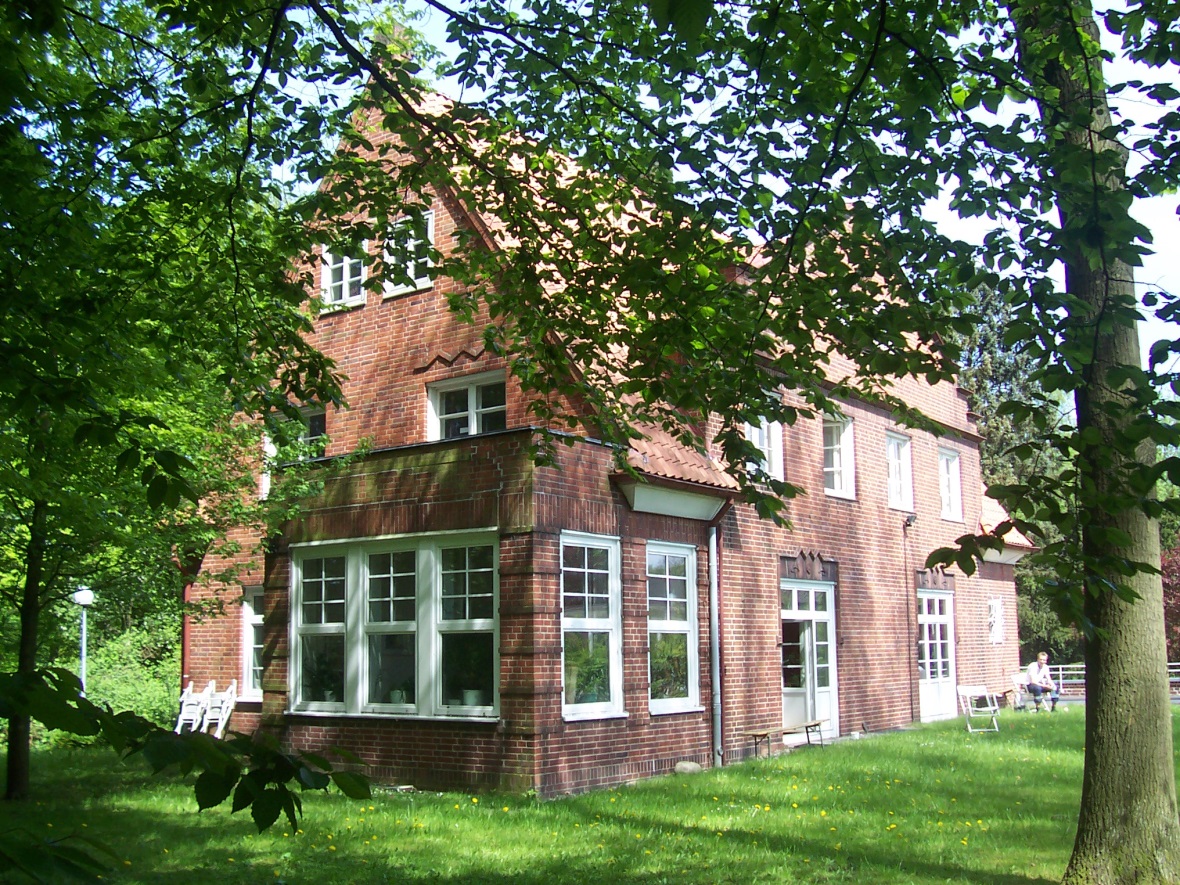 Großes rotes Backsteinhaus hinter Bäumen Rotes Backsteinhaus im Grünen als Immobilienspende
